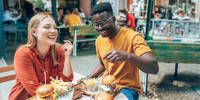 Friends having fun eating burgers and fries at an outdoor restaurant.