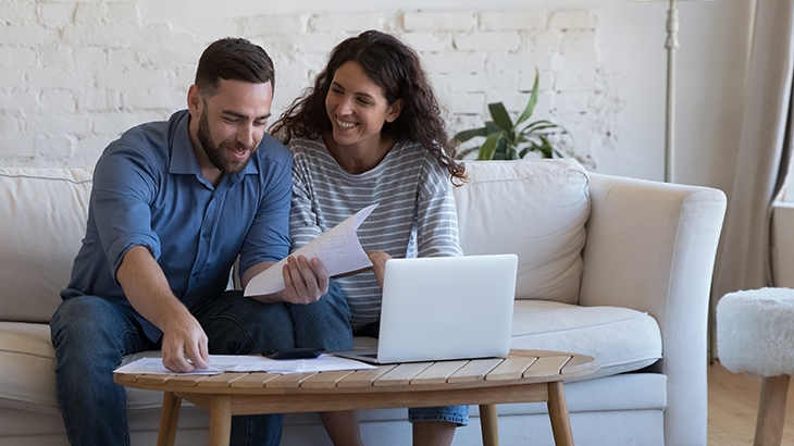 Couple smiling while paying bills on laptop.