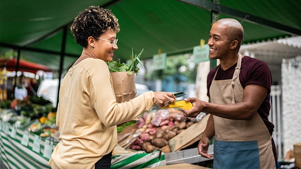 Woman checking out at vegetable stand with a mobile phone.