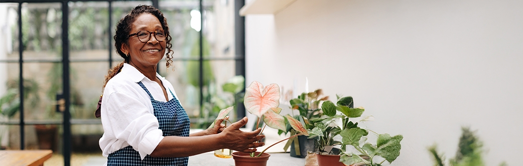 A woman smiling while potting a plant in her shop.