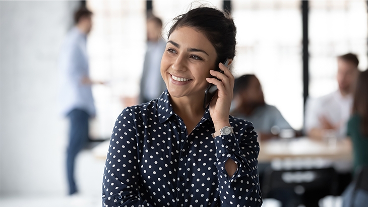 Businesswoman smiling while on her mobile phone in a crowded office. 