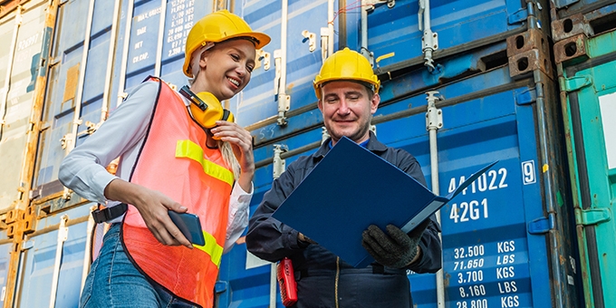 Two people in hardhats talking by shipping containers