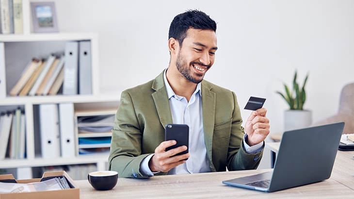 Hombre de negocios sosteniéndo una tarjeta de crédito mientras mira su teléfono movil.