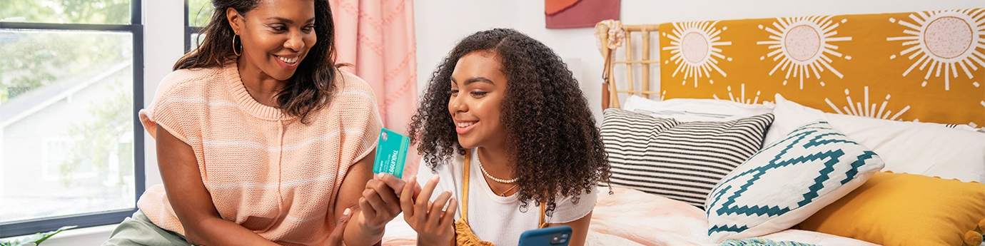 Mother and daughter smiling while looking at the green light app and credit card.