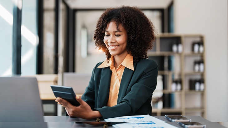 Businesswoman smiling while using a handheld calculator.