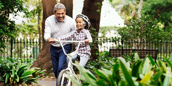 Little girl being taught how to ride a bicycle by her grandfather at the park.