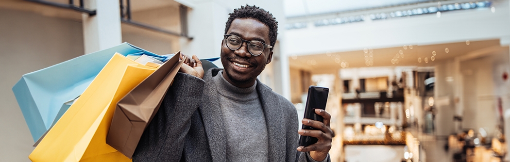 Man with shopping bags holding phone in big shopping mall.
