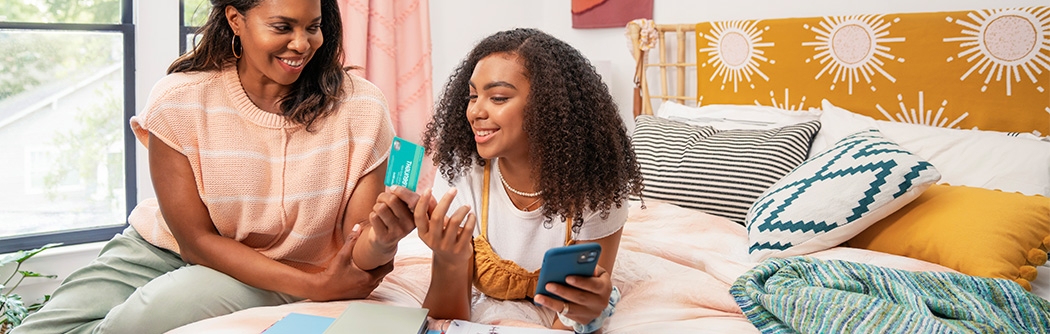 Mother and daughter smiling while looking at the green light app and credit card.
