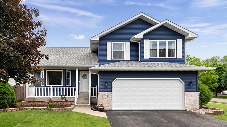 Exterior of a suburban home with blue siding, a white front porch, and white shutters.