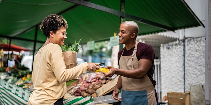 Woman checking out at vegetable stand with a mobile phone.