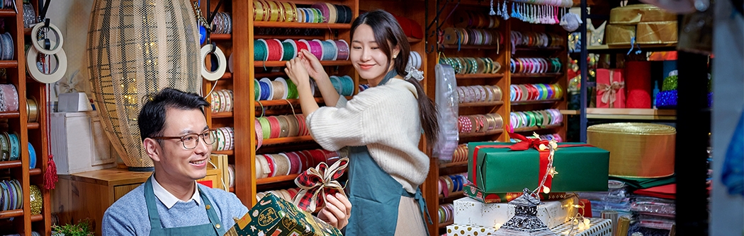A man and woman working in a festive store that sells bright colorful gift wrapping supplies.