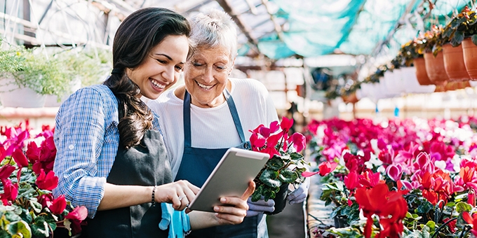 Gardeners with tablet in greenhouse surrounded by flowers