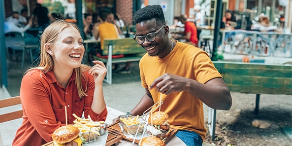 Friends having fun eating burgers and fries at an outdoor restaurant.
