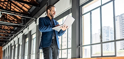 A Businessman walking through an empty office building, looking at his laptop.