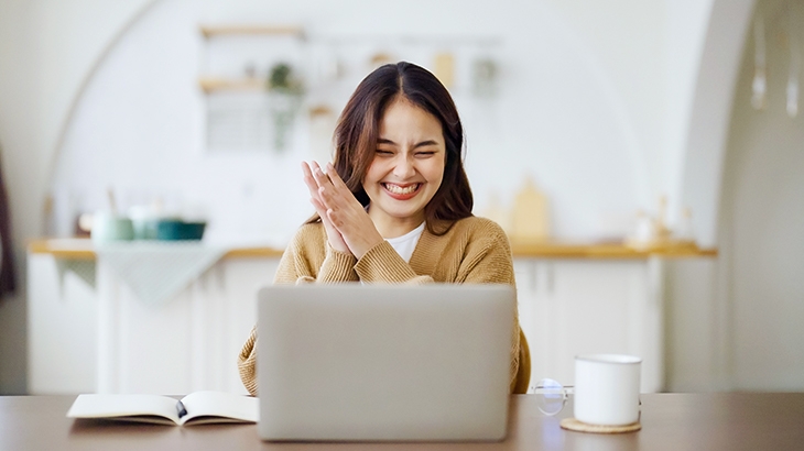 Woman celebrating at laptop, finding great benefits.