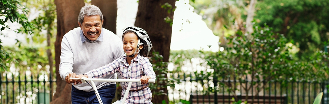Little girl being taught how to ride a bicycle by her grandfather at the park