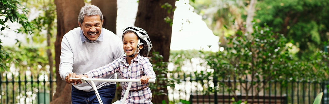 Little girl being taught how to ride a bicycle by her grandfather at the park.