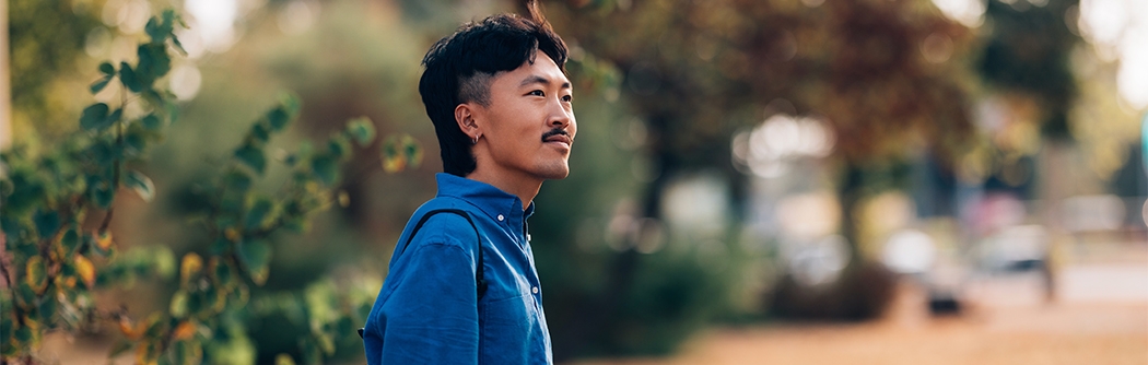 A man in a blue shirt holding a coffee cup while standing outdoors in a park setting.