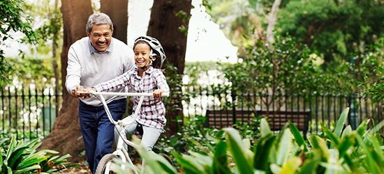 Little girl being taught how to ride a bicycle by her grandfather at the park.