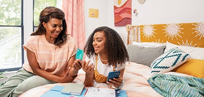 Mother and daughter smiling while looking at the green light app and credit card.