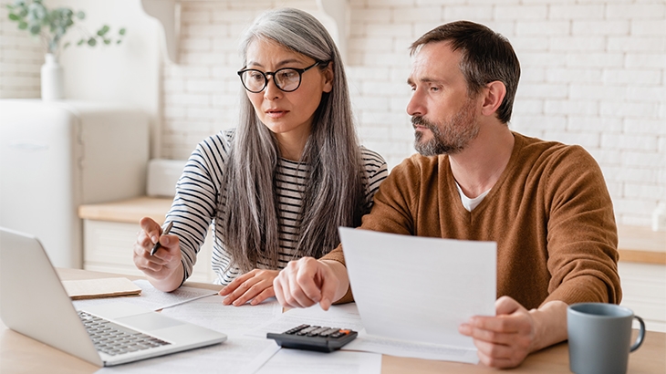 Mature middle-aged couple budgeting with laptop and papers.