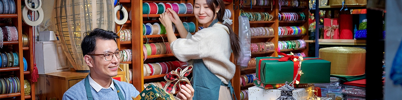 A man and woman working in a festive store that sells bright colorful gift wrapping supplies.