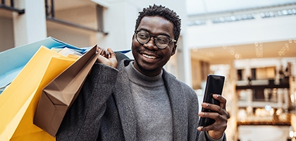 Man with shopping bags holding phone in big shopping mall.