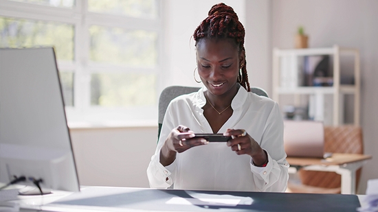 Smiling young woman taking a picture of a check with her smartphone for a mobile deposit in a bright office.