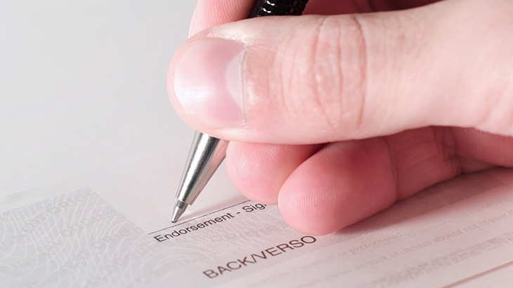 Closeup of hand with pen endorsing the back of a check.