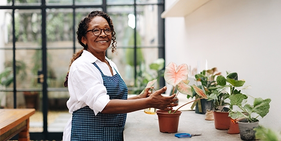A woman smiling while potting a plant in her shop.