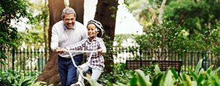 Little girl being taught how to ride a bicycle by her grandfather at the park