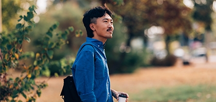 A man in a blue shirt holding a coffee cup while standing outdoors in a park setting.