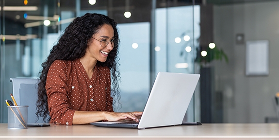 Happy businesswoman in an office working on a laptop.