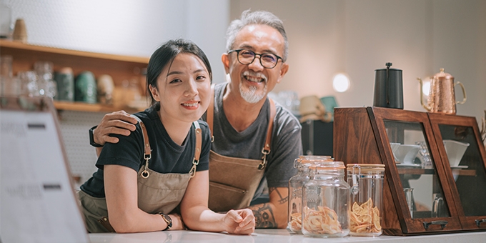 Father and daughter running their cafe, smiling at the counter. 