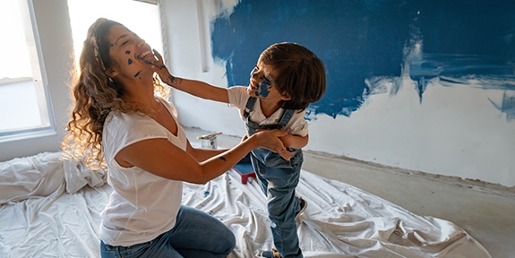 Mother and young son laughing and playing while painting a room.
