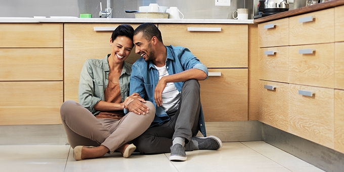 Smiling young couple sitting together on their kitchen floor.