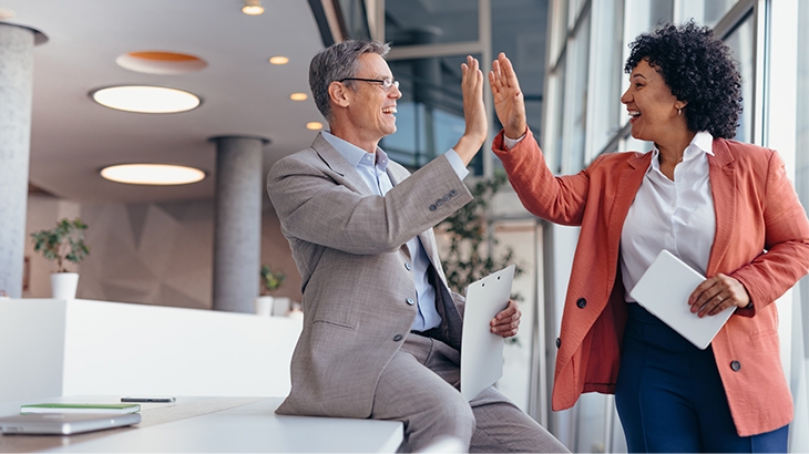 A man and a woman in business attire giving each other a high five in a bright, modern office.