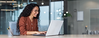 Happy businesswoman in office working on laptop.