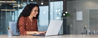 Happy businesswoman in an office working on a laptop.