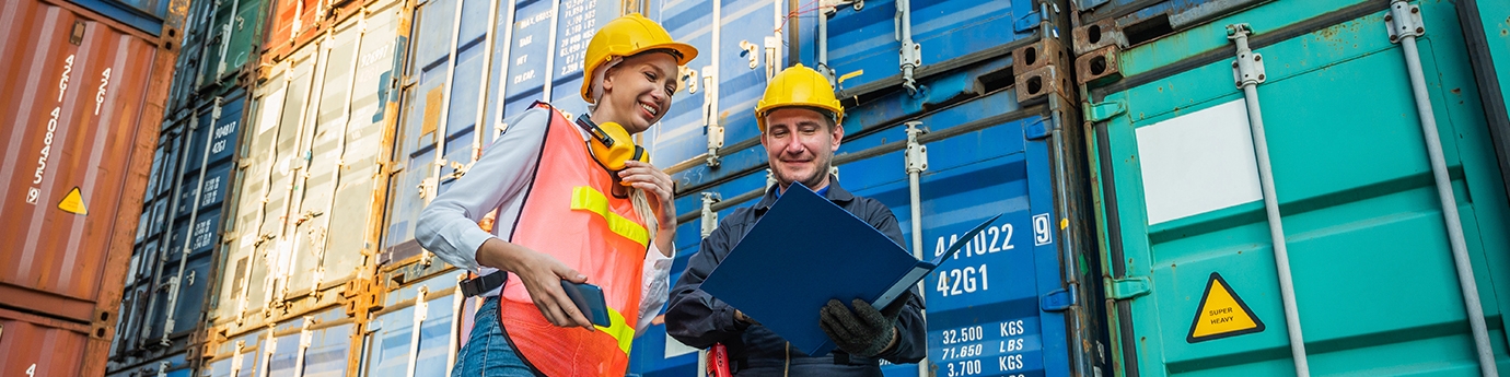 Two people in hardhats talking by shipping containers