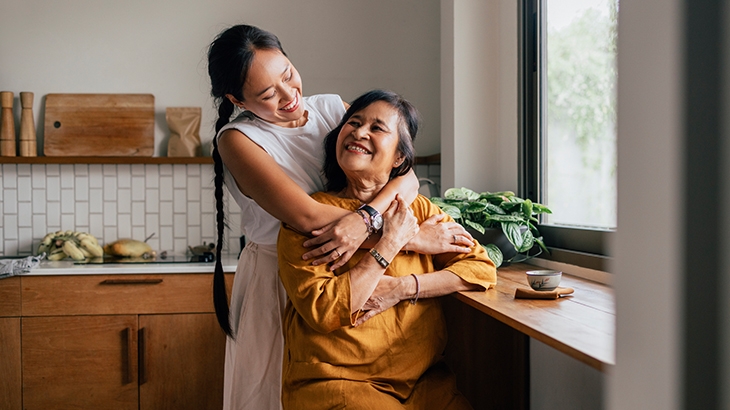Elderly woman smiling and daughter hugging her.