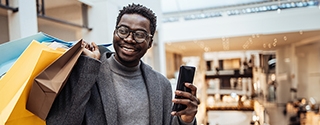 Man with shopping bags holding phone in big shopping mall.
