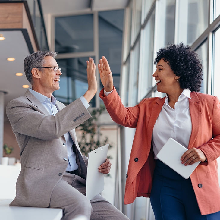 A man and a woman in business attire giving each other a high five in a bright, modern office.