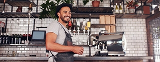 Happy young bar owner standing at the counter.