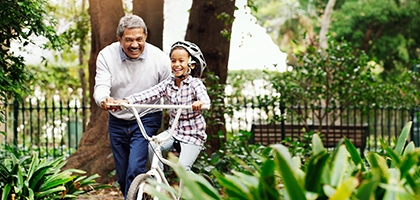 Little girl being taught how to ride a bicycle by her grandfather at the park.