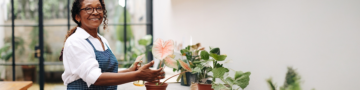 A woman smiling while potting a plant in her shop.