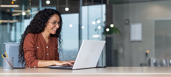 Happy businesswoman in an office working on a laptop.