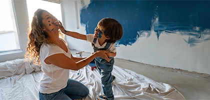 Mother and young son laughing and playing while painting a room.