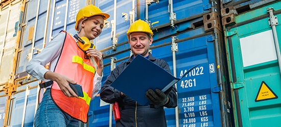 Two people in hardhats talking by shipping containers