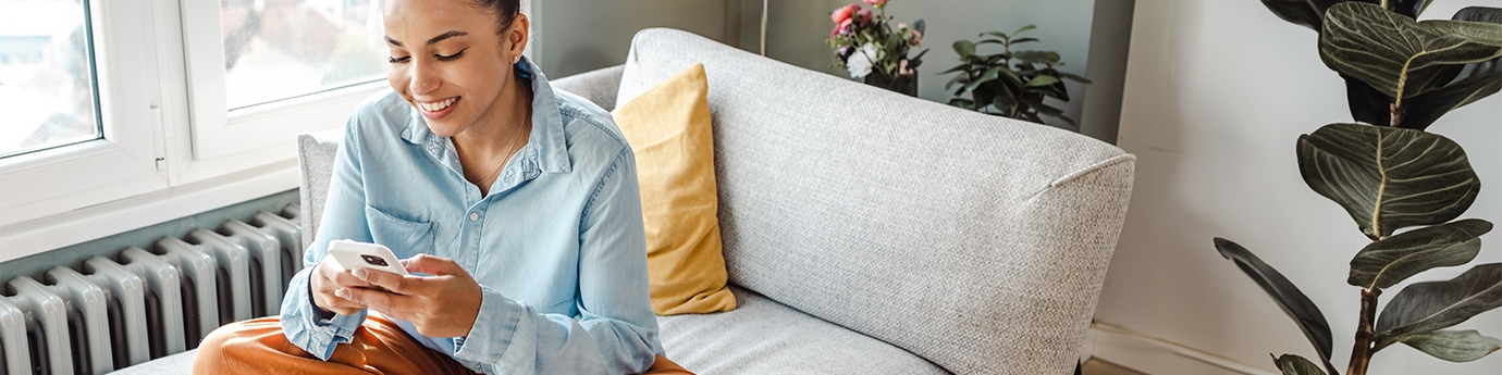 Woman on her mobile phone while sitting cross-legged on a couch.